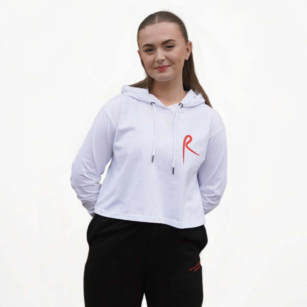 White cropped hoodie with a red arabesque symbol on the front and the Royal Academy of Dance logo on the cuff, paired with black pants.