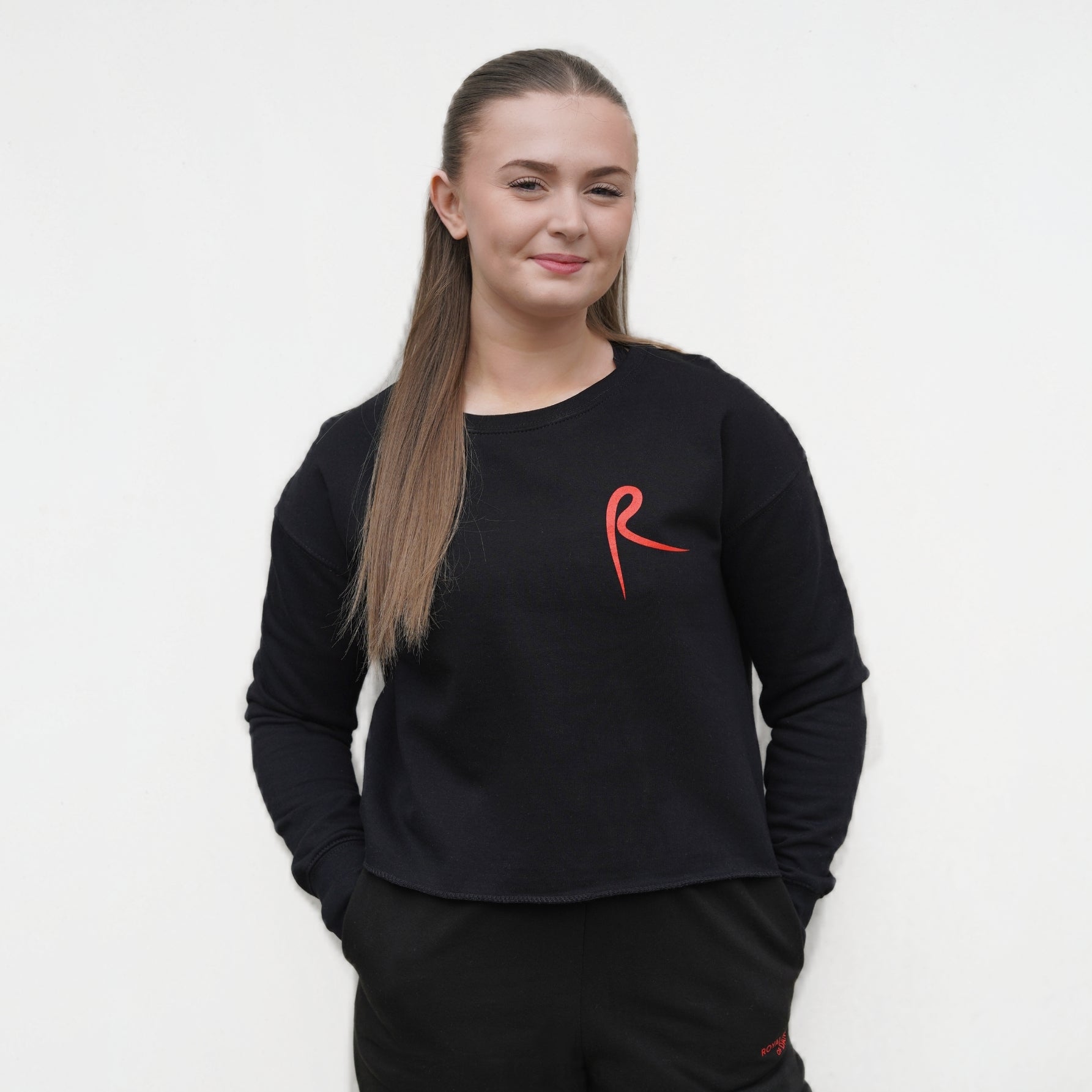 Black cropped sweatshirt with a red arabesque symbol on the front. Royal Academy of Dance. 