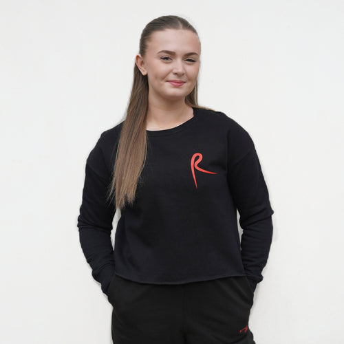 Black cropped sweatshirt with a red arabesque symbol on the front. Royal Academy of Dance. 