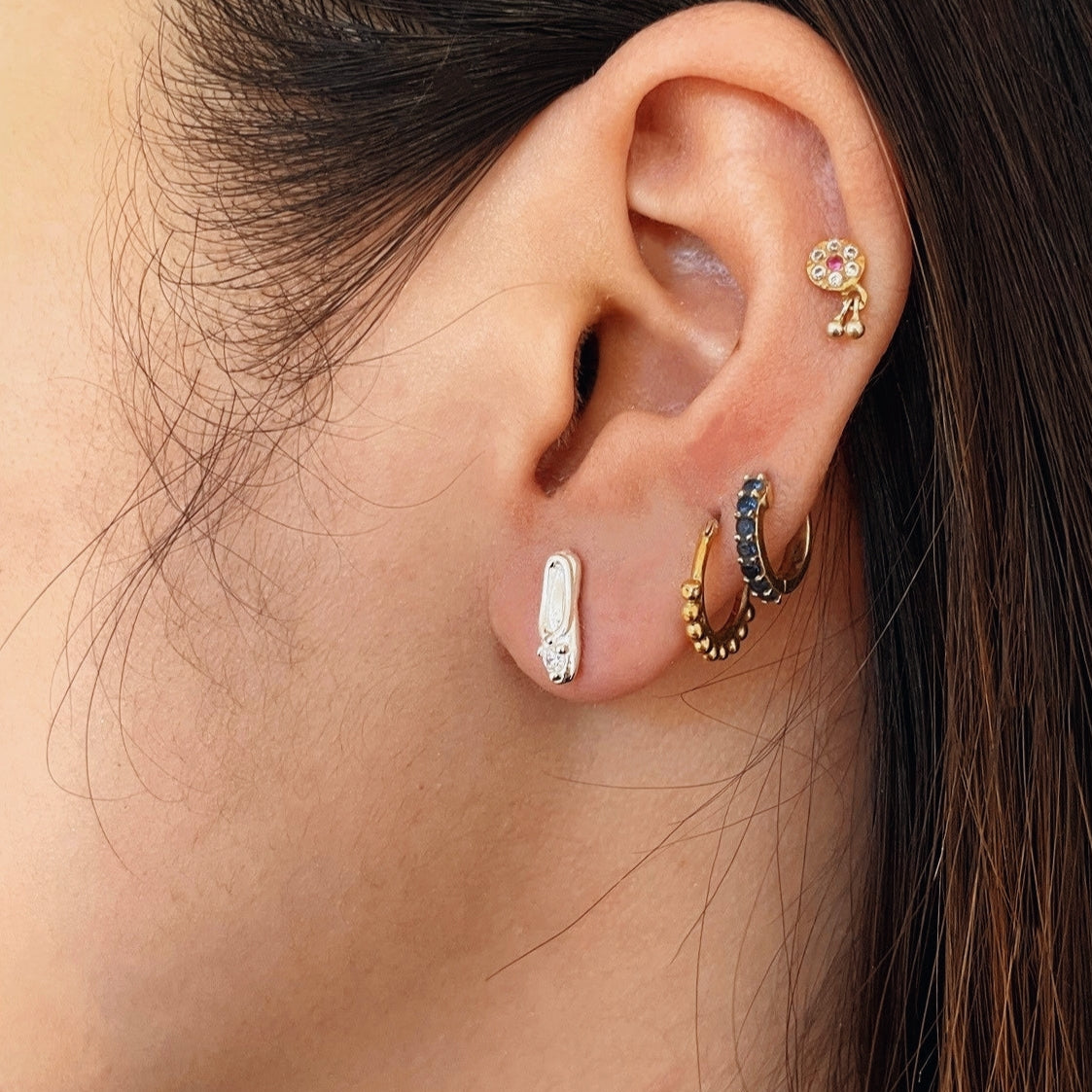 A pair of classic sterling silver stud earrings, each crafted in the shape of a petite, elegant ballet slipper. A single, brilliant cubic zirconia is set at top of the shoe, acting as a sparkling focal point. These dainty studs offer a subtle and refined nod to ballet, perfect for everyday wear. Designed by Royal Academy of Dance. Made in the UK.