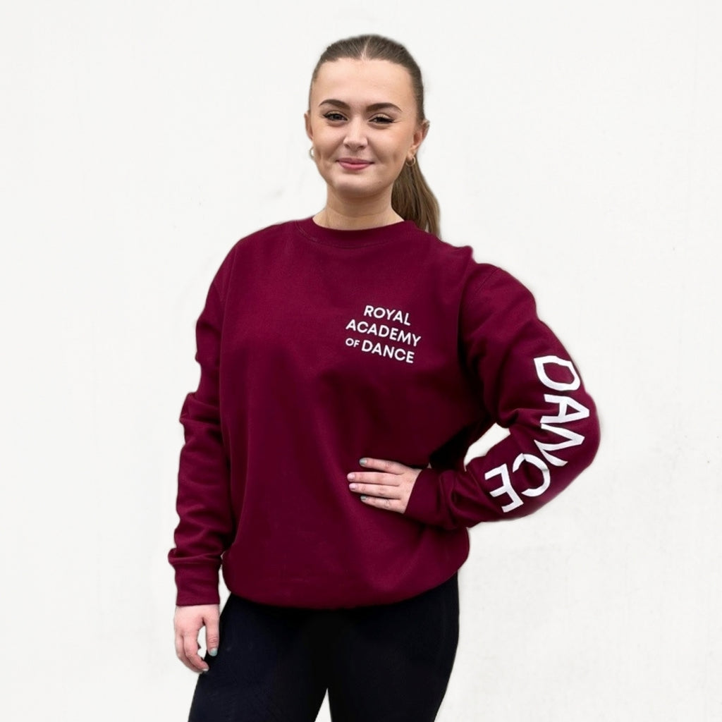 Burgundy sweatshirt with the white 'DANCE' printed on the left arm and the 'Royal Academy of Dance' logo on the left chest.