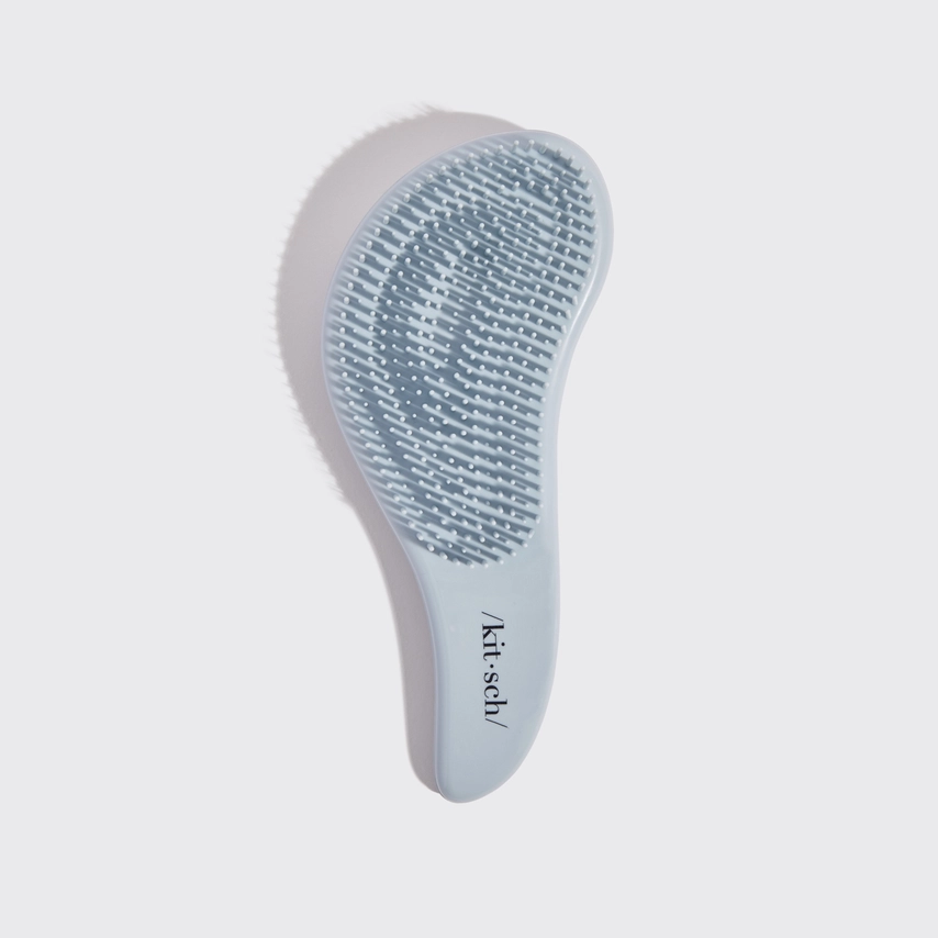 Blue grooming brush with textured surface on a light gray background