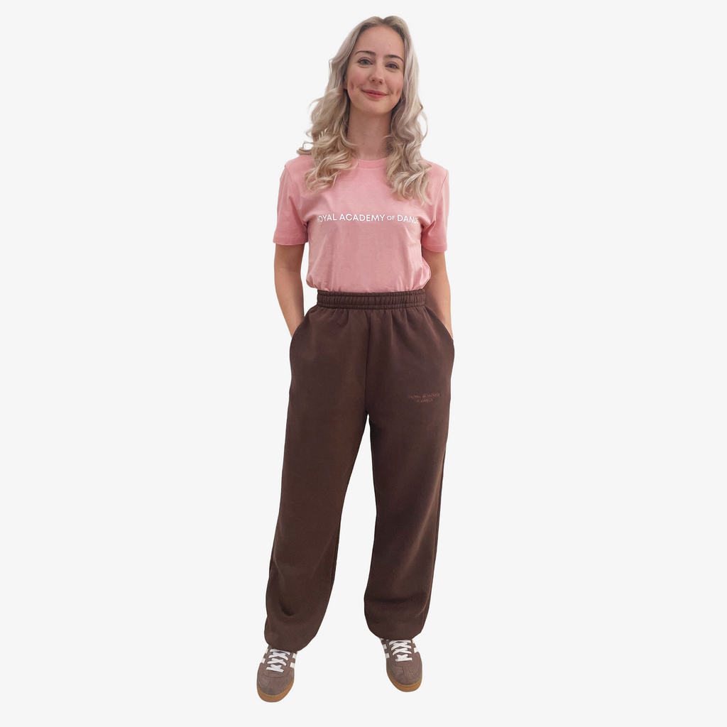 Woman wearing a pink t-shirt with 'Royal Academy of Dance' logo in white and brown jogger