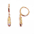 A pair of gold-plated sterling silver huggie hoop earrings, designed to hug the earlobe closely. From the curved base of each hoop dangles a delicate charm in the shape of a classical ballet slipper. The shoe charm is meticulously detailed, featuring sparkling cubic zirconia stone catching the light with each subtle movement. The earrings combine minimalist huggie style with a playful, sparkling tribute to dance. Designed by Royal Academy of Dance. Made in the UK