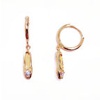 A pair of gold-plated sterling silver huggie hoop earrings, designed to hug the earlobe closely. From the curved base of each hoop dangles a delicate charm in the shape of a classical ballet slipper. The shoe charm is meticulously detailed, featuring sparkling cubic zirconia stone catching the light with each subtle movement. The earrings combine minimalist huggie style with a playful, sparkling tribute to dance. Designed by Royal Academy of Dance. Made in the UK