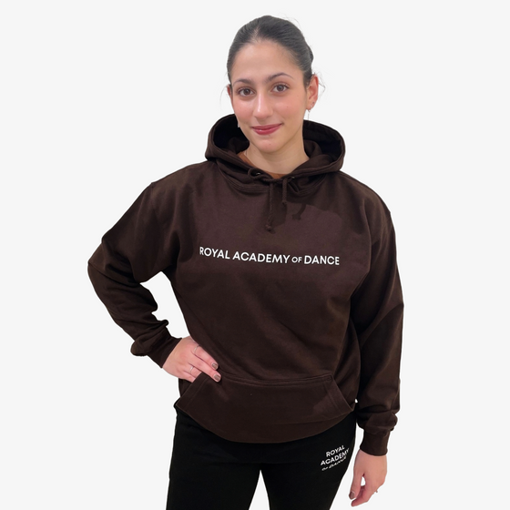 Woman wearing a brown hoodie with 'Royal Academy of Dance' text 