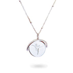 A close-up of a delicate spinning disc pendant on a necklace. The circular disc is shown mid-spin, creating a slight blur that hints at its movement. One side features a finely engraved ballerina poised in a graceful arabesque, while the opposite side reveals the formal crest of the Royal Academy of Dance. The disc hangs from a sleek chain, capturing a moment of dynamic elegance where dance and heritage revolve together.