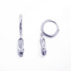 A pair of sterling silver huggie hoop earrings, designed to hug the earlobe closely. From the curved base of each hoop dangles a delicate charm in the shape of a classical ballet slipper. The shoe charm is meticulously detailed, featuring sparkling cubic zirconia stone, catching the light with each subtle movement. The earrings combine minimalist huggie style with a playful, sparkling tribute to dance. Designed by Royal Academy of Dance. Made in the UK